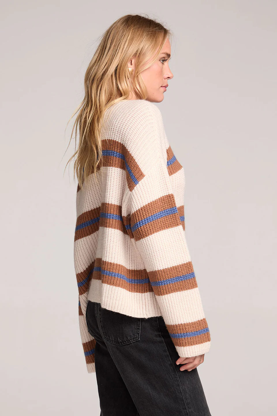 Woman wearing a cream sweater with brown and blue stripes on a plain background