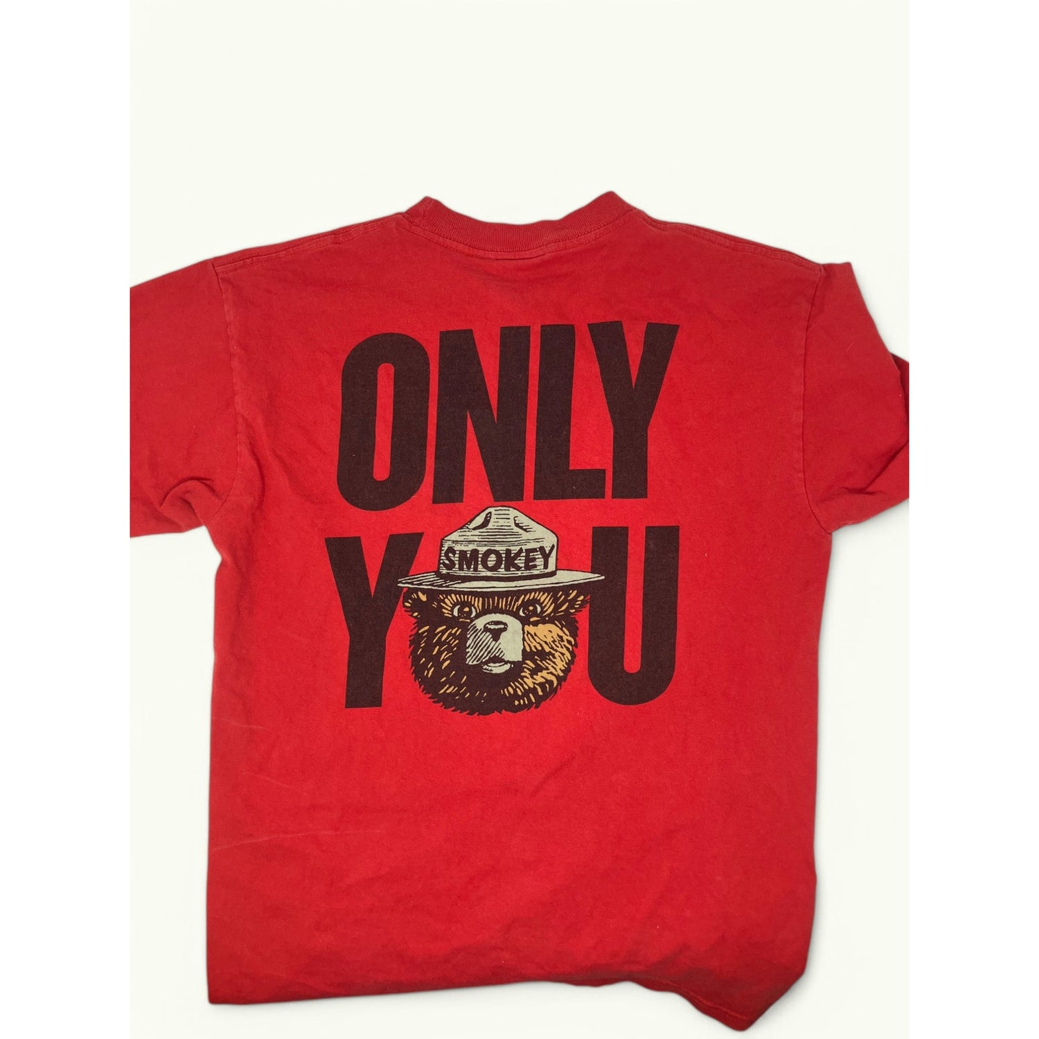 A red short-sleeve t-shirt laid flat, featuring a large black graphic on the back that reads 'ONLY YOU' with a Smokey Bear illustration integrated into the lettering.