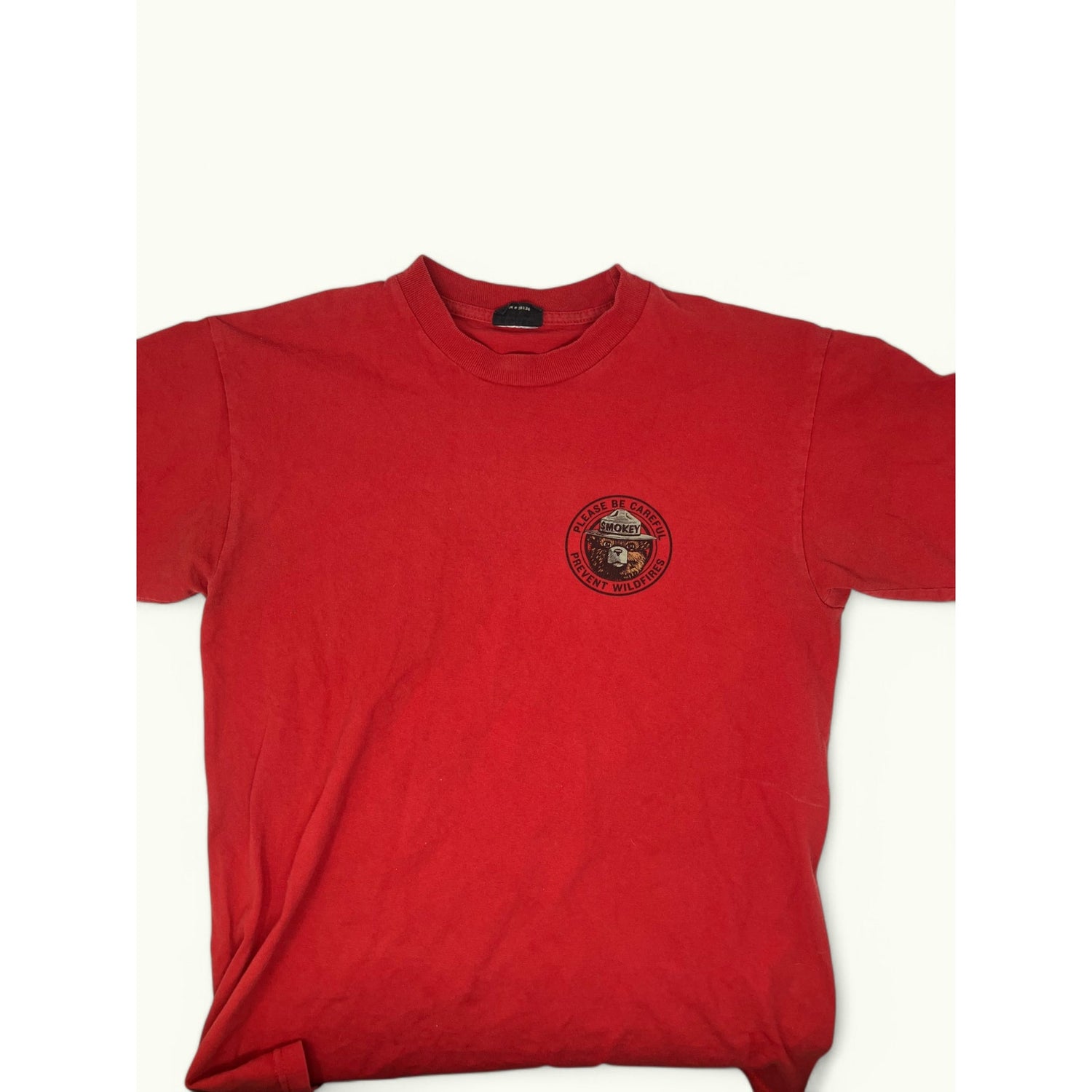 A red short-sleeve crewneck t-shirt with a circular embroidered logo on the left chest, displayed flat against a light off-white background.
