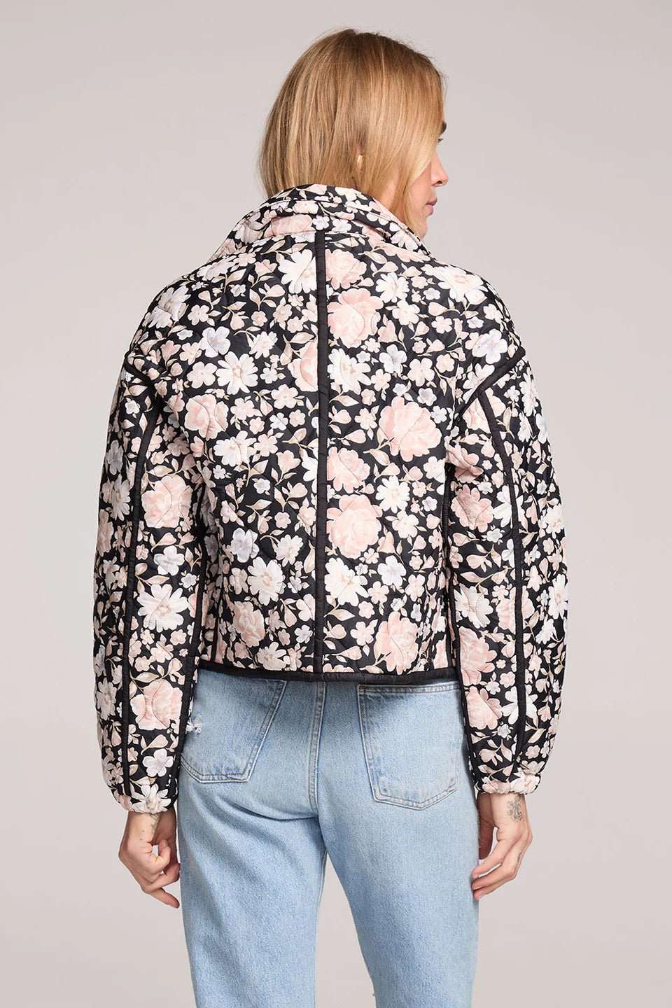 Person wearing a floral jacket and light blue jeans on a plain background