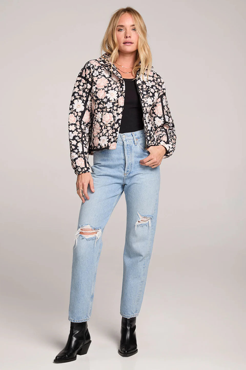 Woman wearing a floral jacket, black top, and light blue jeans on a plain background