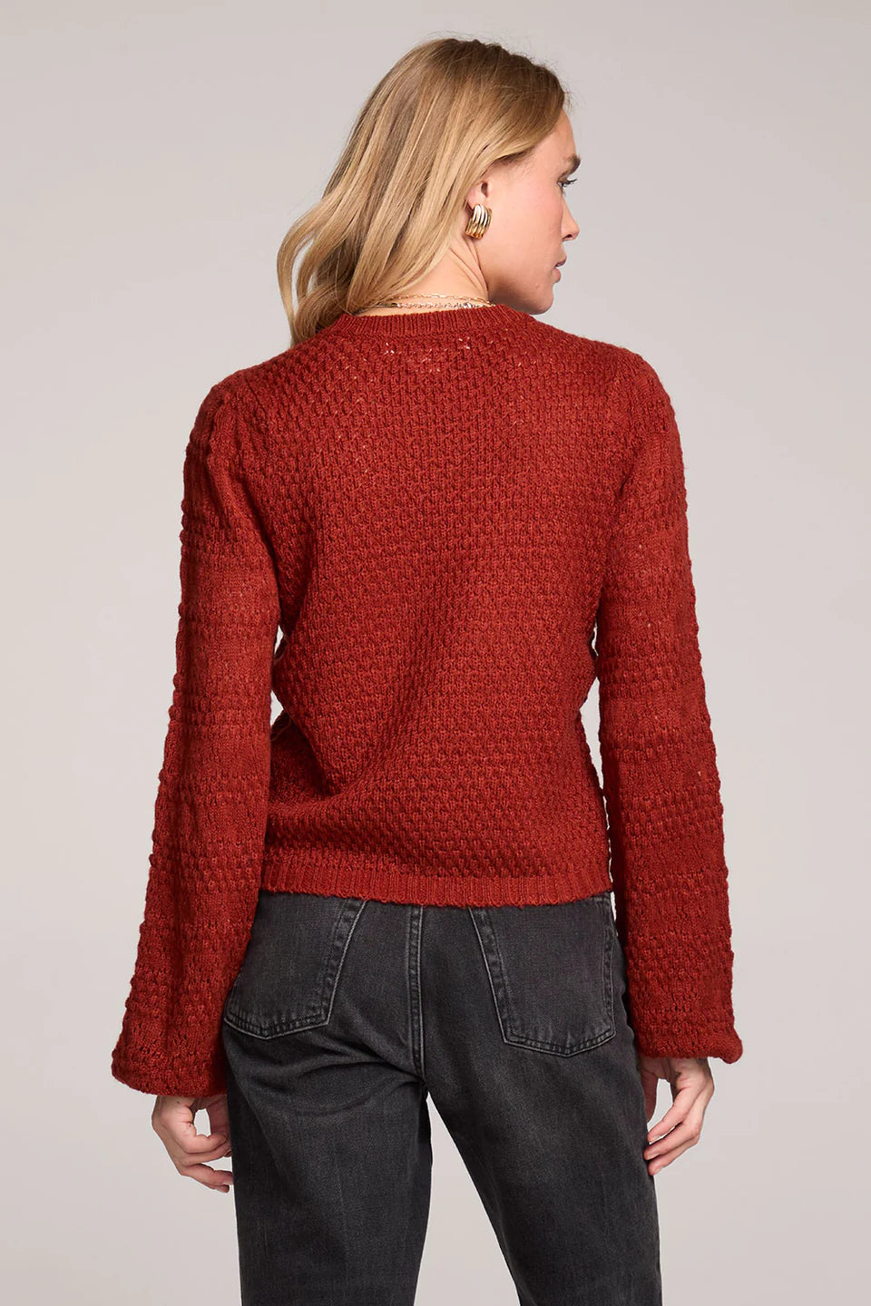 Person wearing a red textured sweater and dark jeans on a plain background