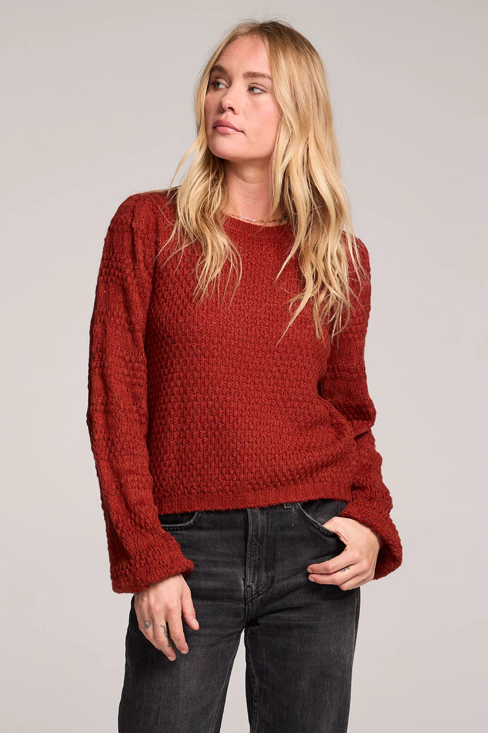 Woman wearing a red sweater and dark jeans against a plain background