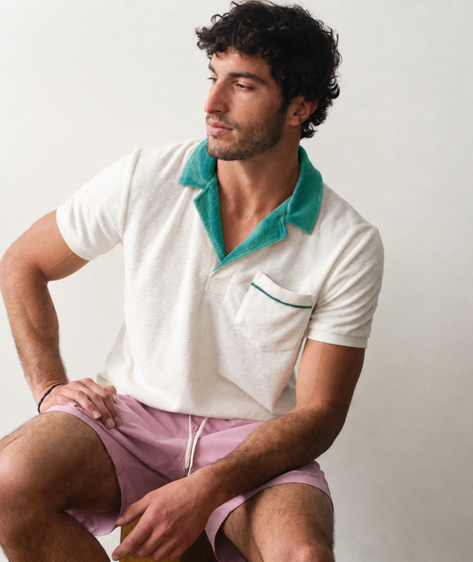 Man wearing a white polo shirt with green collar and pink shorts on a plain background