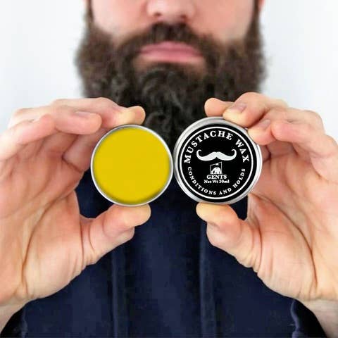 Person holding two containers of moustache wax with a visible brand logo.