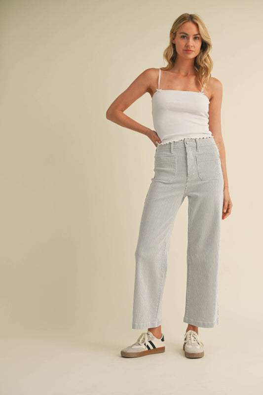 Woman wearing a white tank top and light gray jeans against a beige background