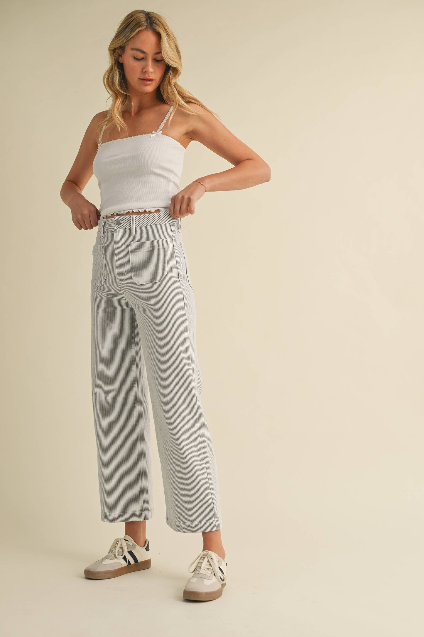 Woman wearing a white tank top and light blue jeans on a beige background