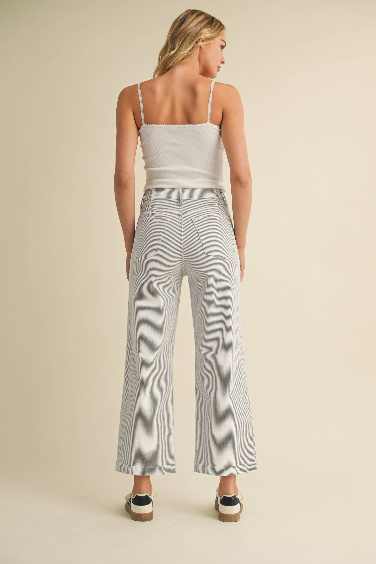 Woman wearing a white top and light gray wide-leg pants on a beige background
