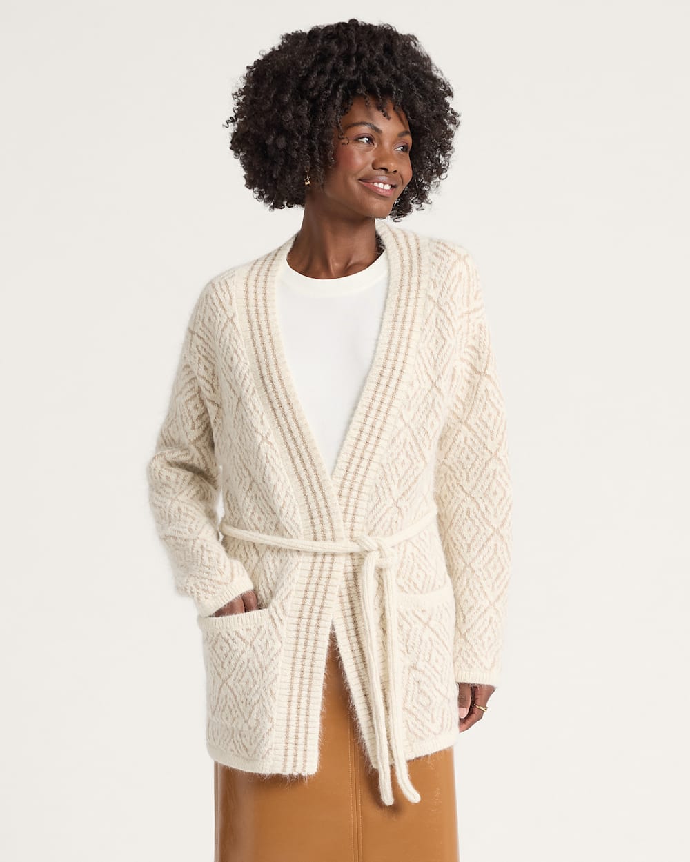 Woman wearing a cream-colored cable knit cardigan on a plain background