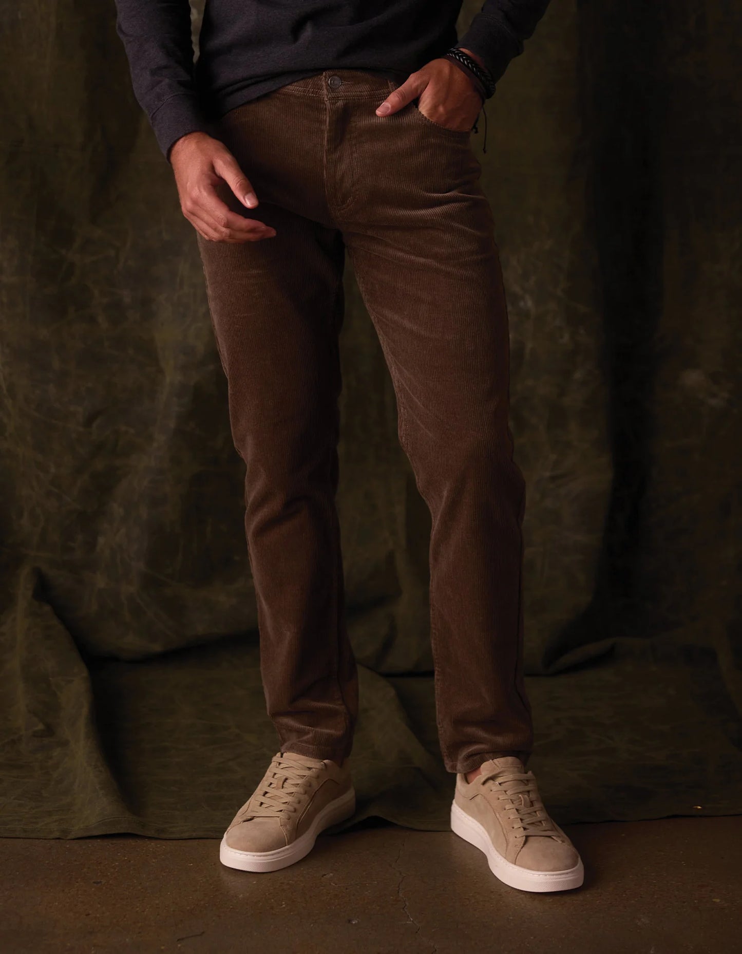 Person wearing brown pants and beige shoes against a dark background