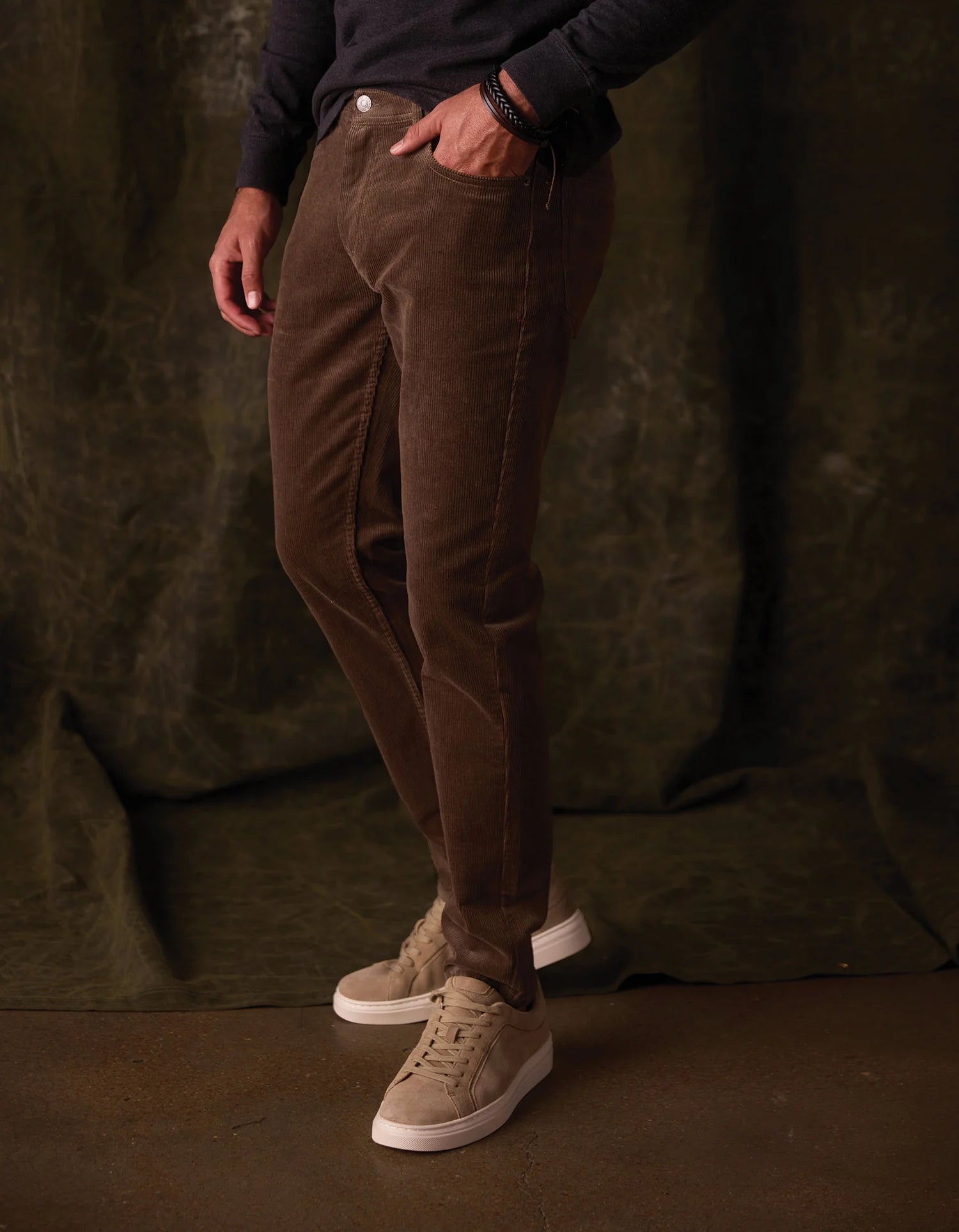 Person wearing brown corduroy pants and beige sneakers against a dark background