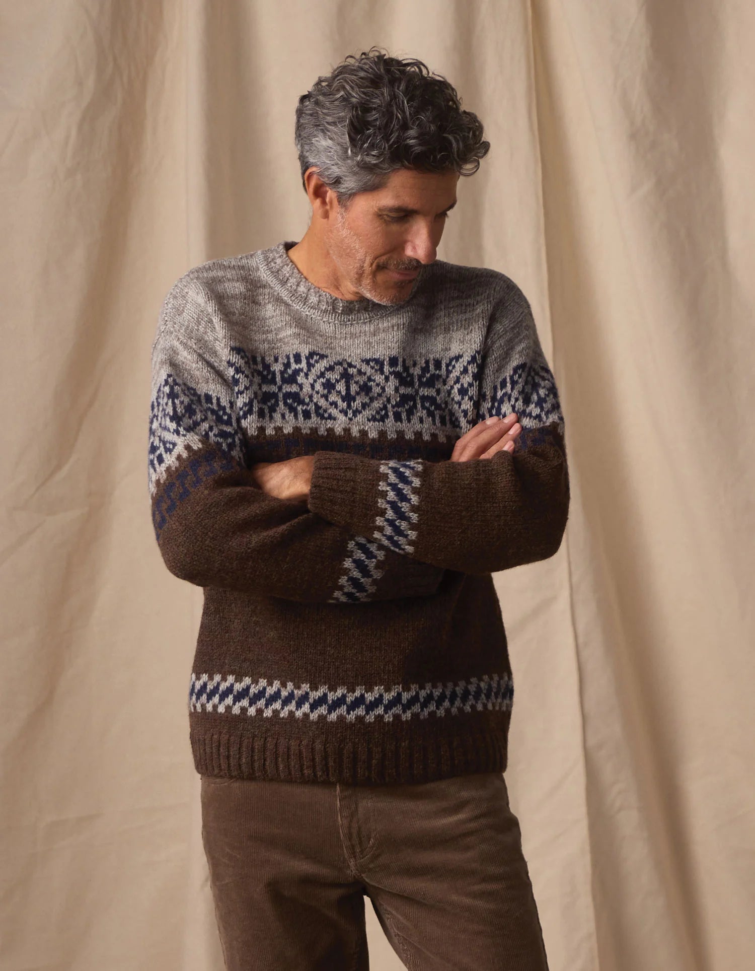 Man wearing a patterned sweater against a beige curtain