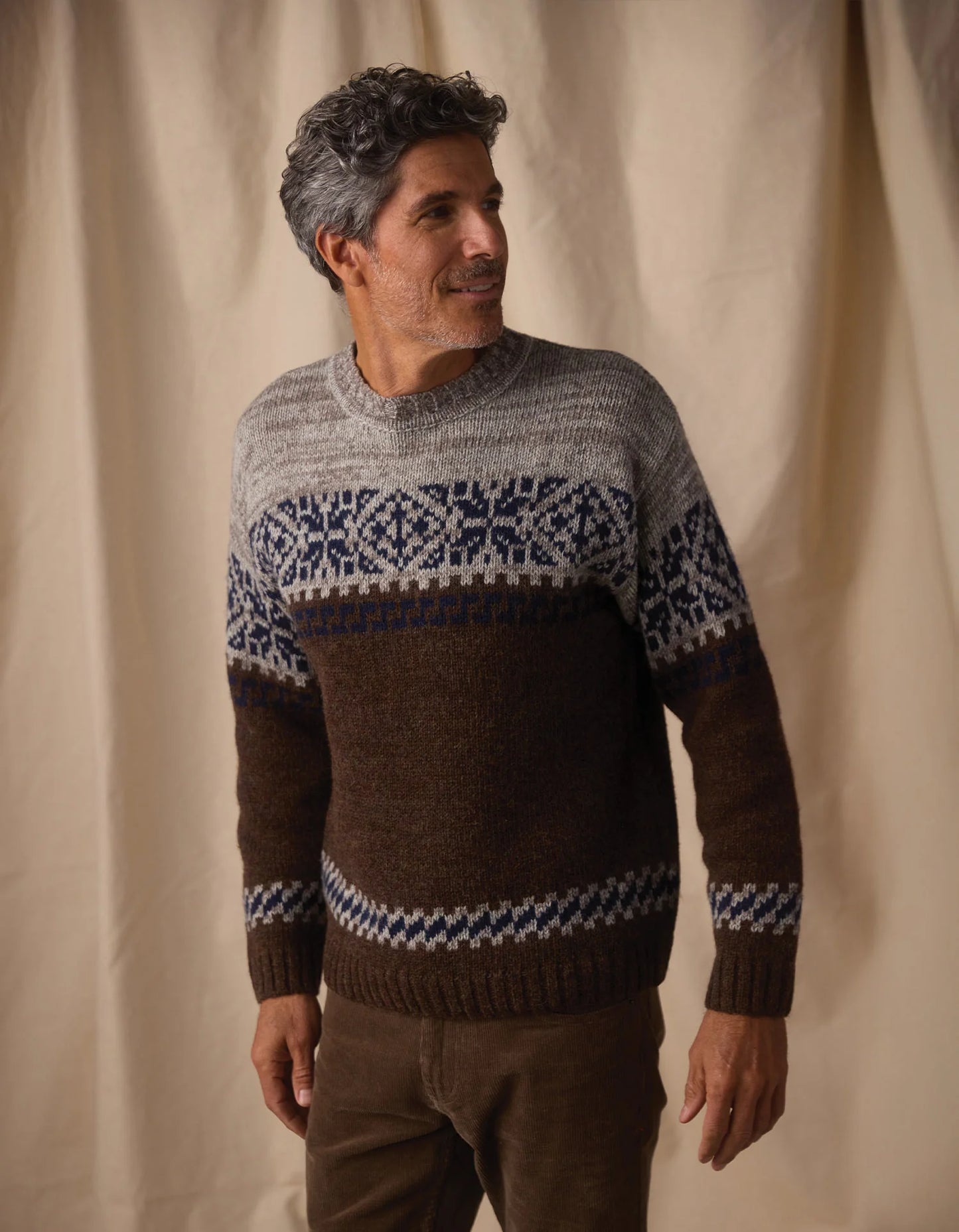 Man wearing a patterned sweater against a beige curtain