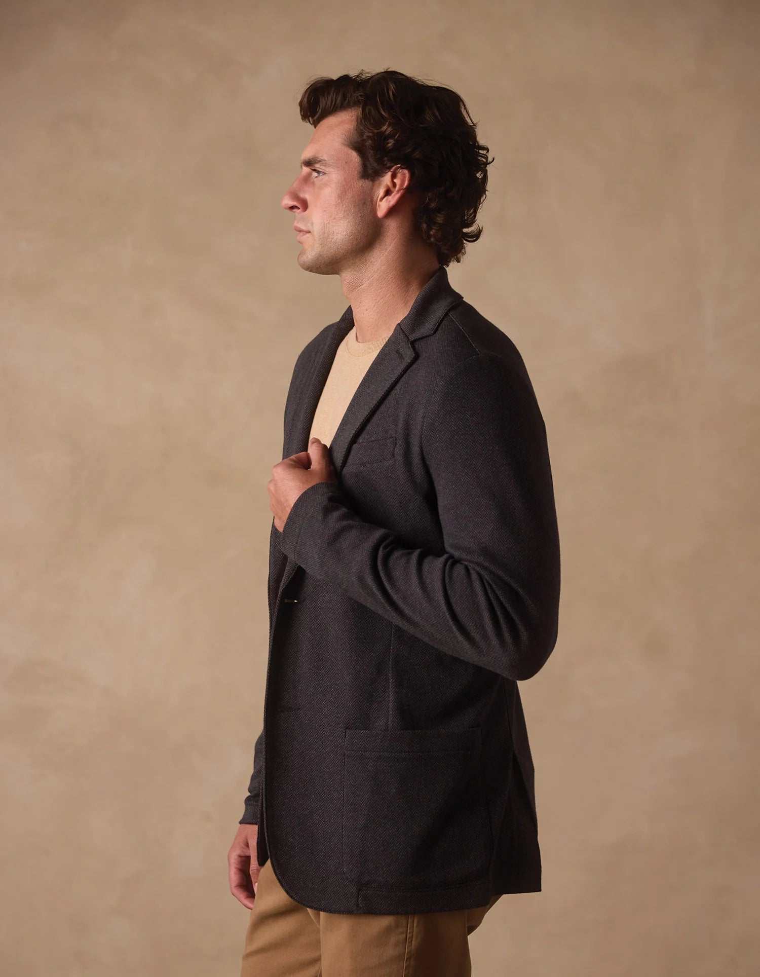 Man wearing a dark blazer over a beige shirt against a beige background