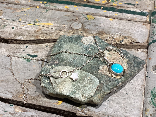 Necklace with a turquoise pendant and star charm on a stone surface