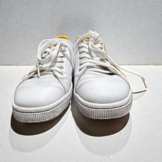 Pair of white sneakers with yellow accents on a light gray background