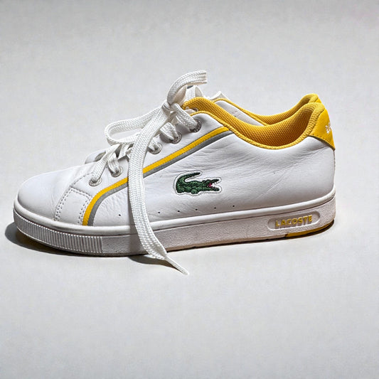 White sneaker with yellow accents and a visible brand logo on a light gray background