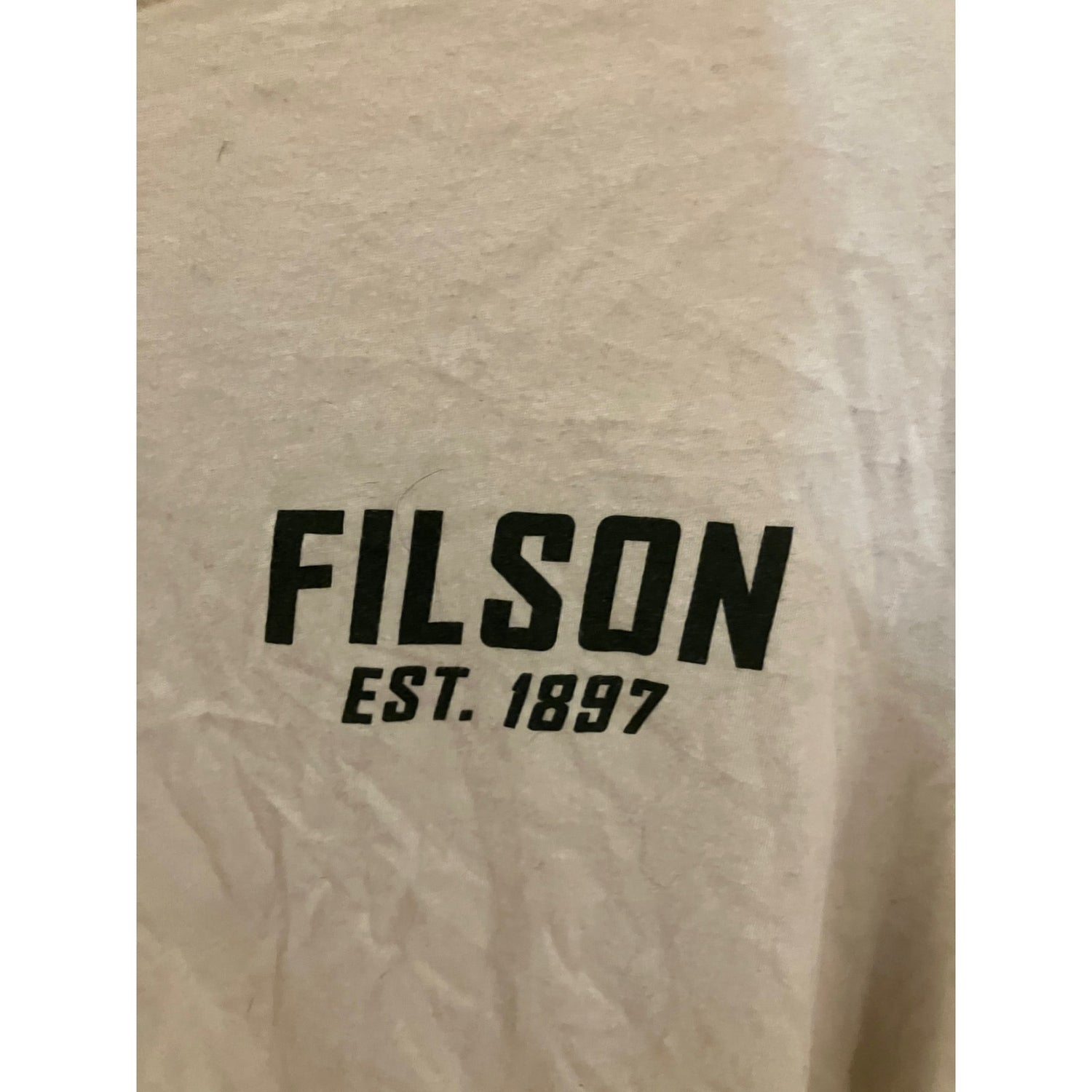 Close-up of a beige or off-white textured surface with the brand name FILSON printed in bold black letters and 'EST. 1897' underneath.