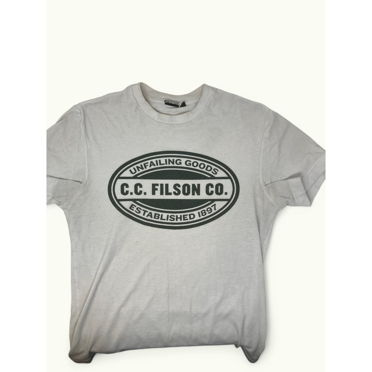 A light gray short-sleeve t-shirt with a black oval graphic on the chest that reads 'UNFAILING GOODS C.C.