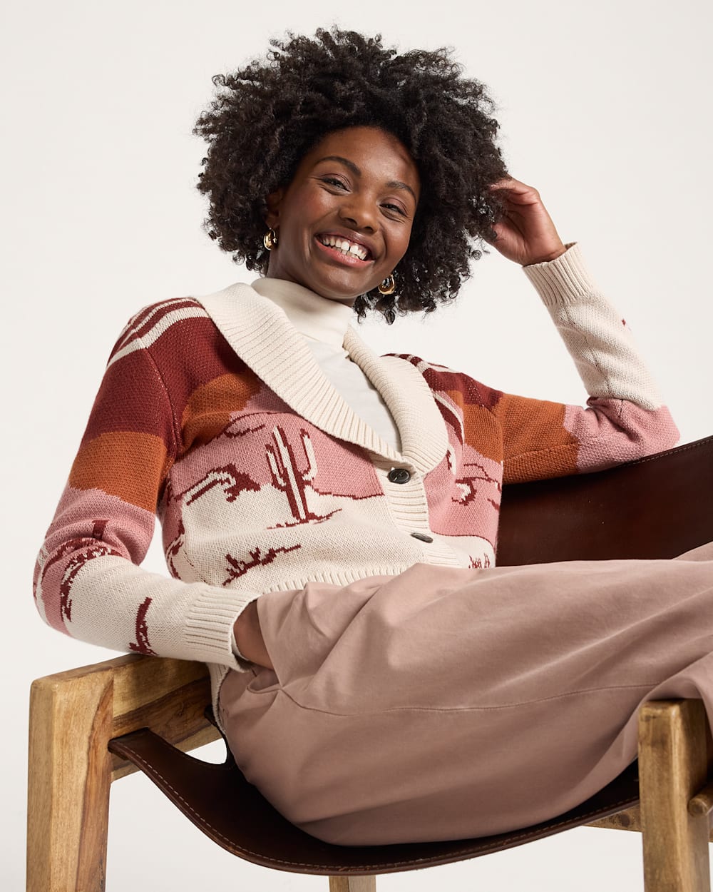 Woman wearing a patterned sweater sitting on a chair with a plain background