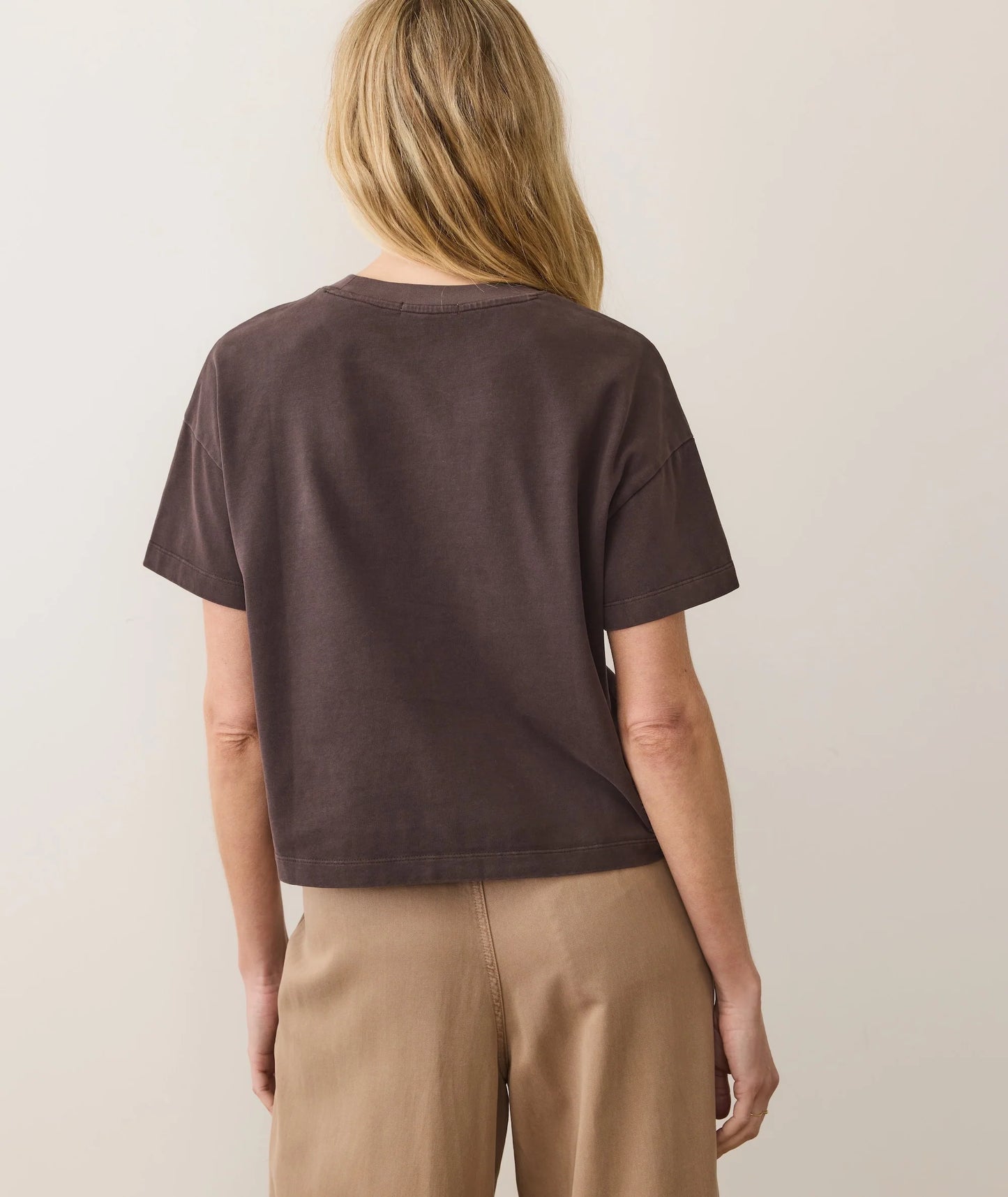 Person wearing a brown t-shirt and beige pants against a plain background