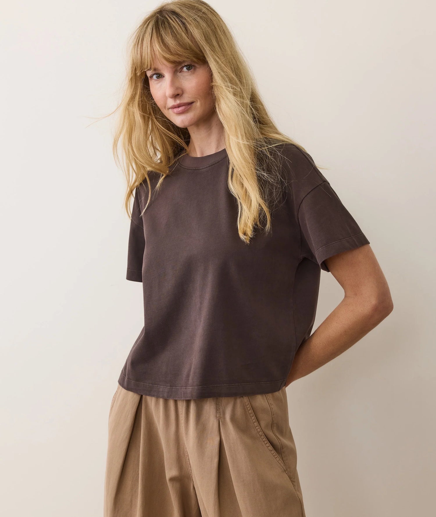 Woman wearing a brown t-shirt and beige pants against a plain background