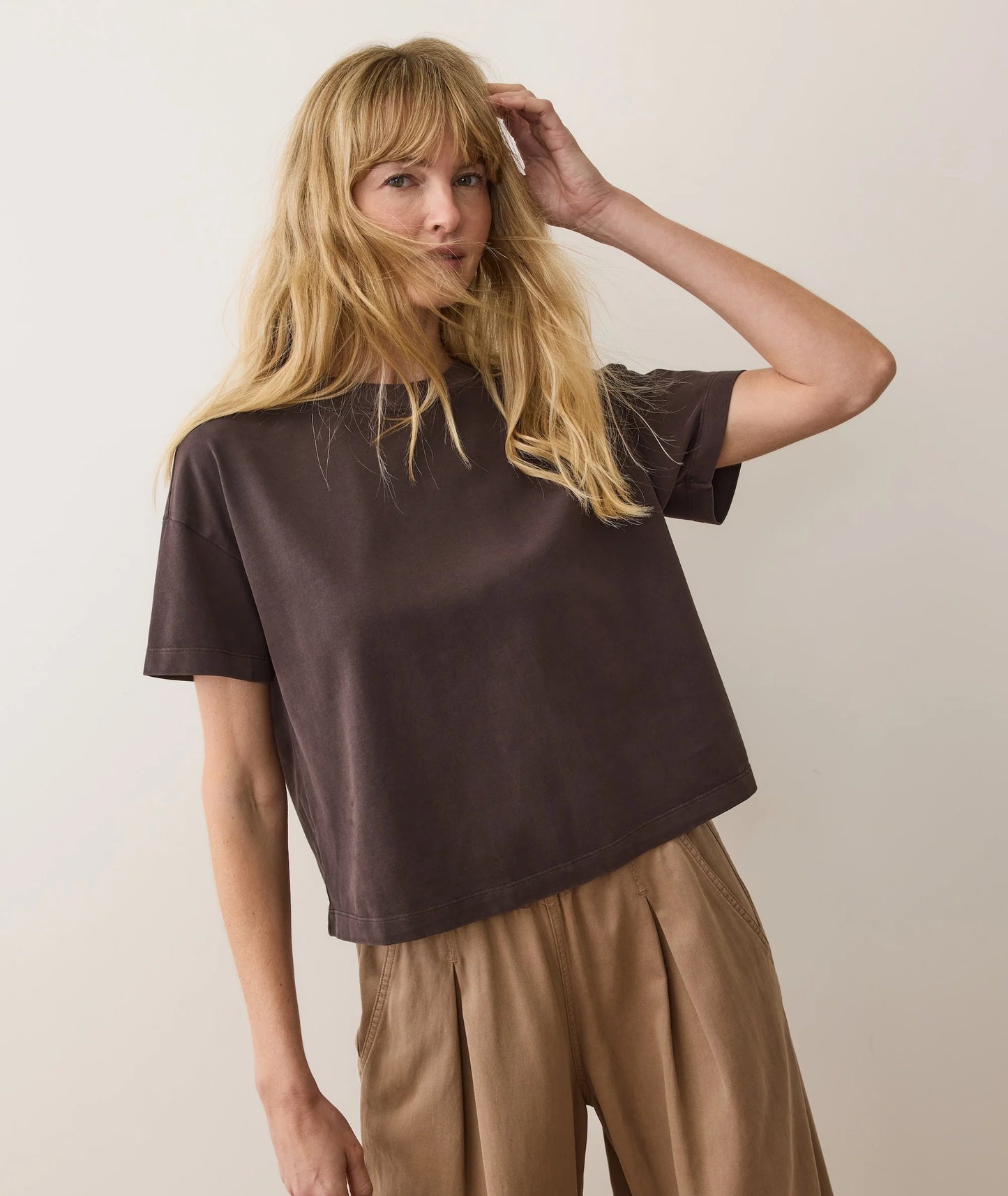 Woman wearing a brown t-shirt and beige pants against a plain background