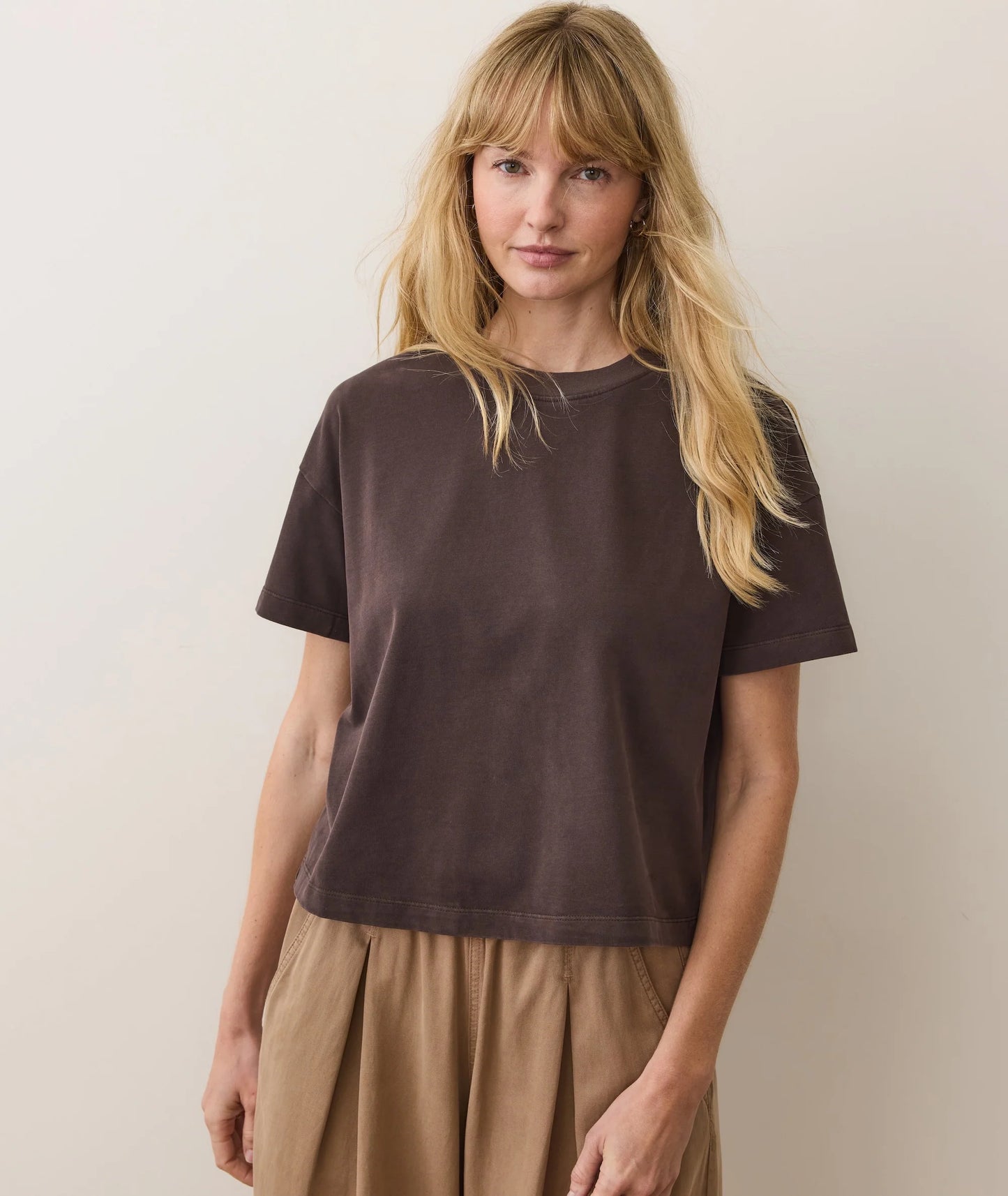 Woman wearing a brown t-shirt and beige pants against a plain background