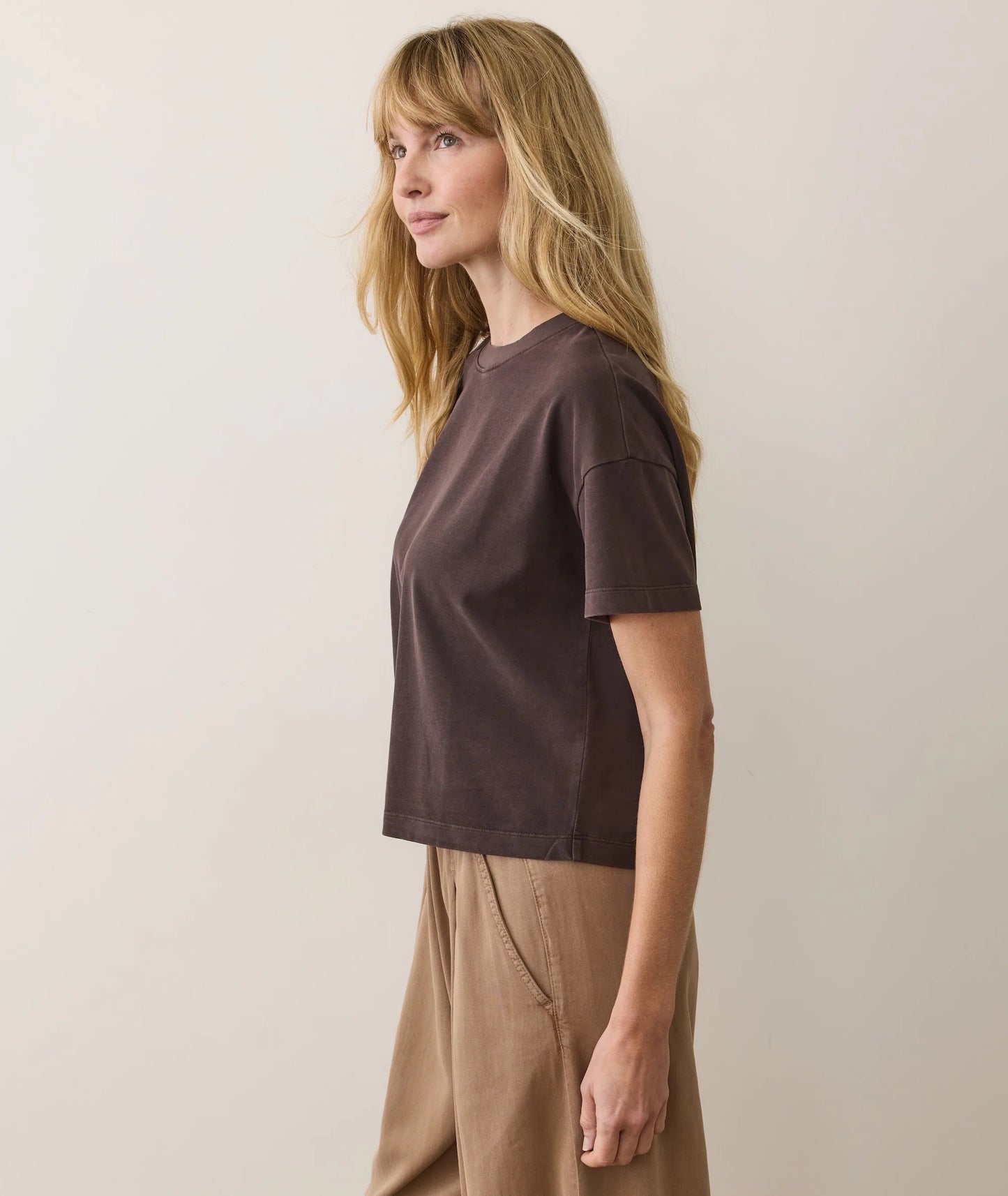Woman wearing a brown t-shirt and beige pants against a plain background