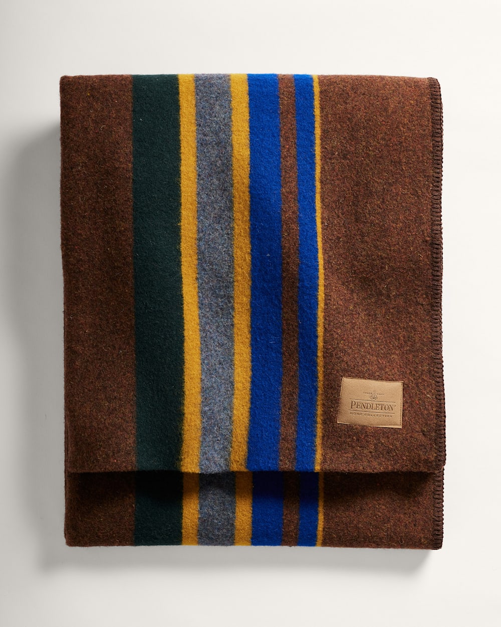 Folded brown blanket with multicolored stripes and a brand label on a white background
